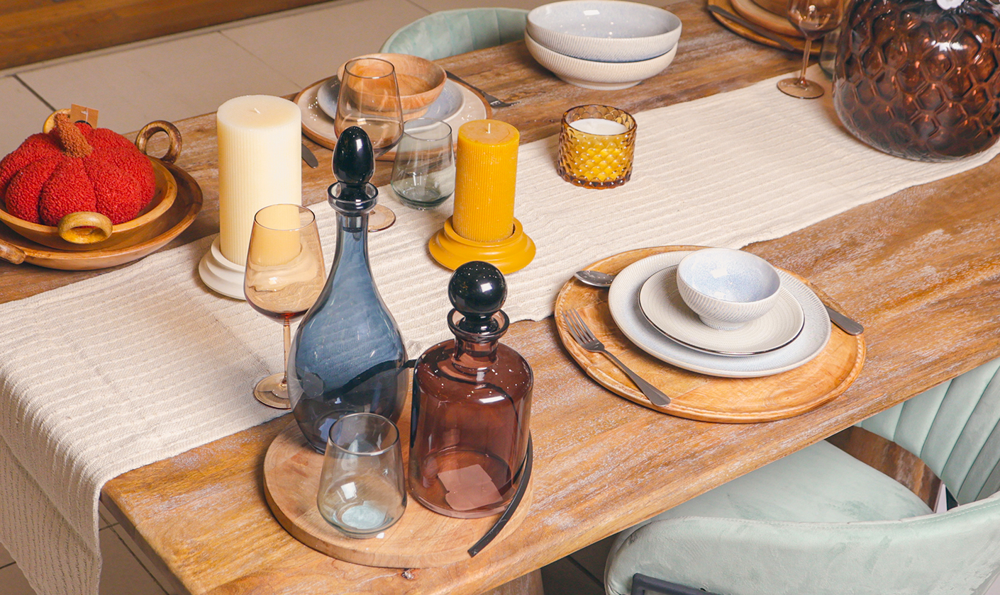 Modern tableware set displayed on a dining table with plates, bowls, glasses, and candles.